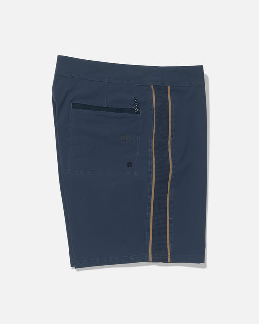 Discover the Salty Crew Channel 18″ Apex Boardshort in navy, featuring a back pocket, zipper, and button. Crafted from quick-dry fabric for all-day comfort, these boardshorts showcase a vertical tan and dark blue stripe along the right side. Designed with a straight-leg performance silhouette, they are displayed flat against a white background.