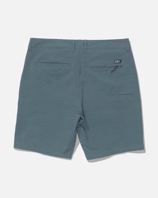 Back view of the Salty Crew Drifter 19″ Slub Hybrid shorts in Mid Ocean blue, showcasing belt loops, two back pockets—including one with a zipper—and a small black Salty Crew logo patch above the right pocket, crafted from recycled performance fabric with 4-way stretch for superior comfort and mobility, set against a white background.