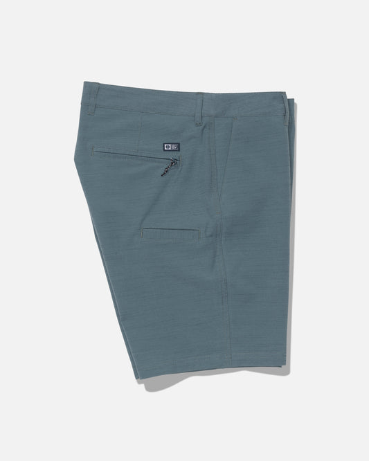 A pair of Salty Crew Drifter 19″ Slub Hybrid shorts in Mid Ocean lies flat on a white background, displaying the back side with a zippered pocket and an additional horizontal slit pocket. Made from recycled performance fabric, these shorts deliver quick-dry comfort and 4-way stretch for all-day ease.