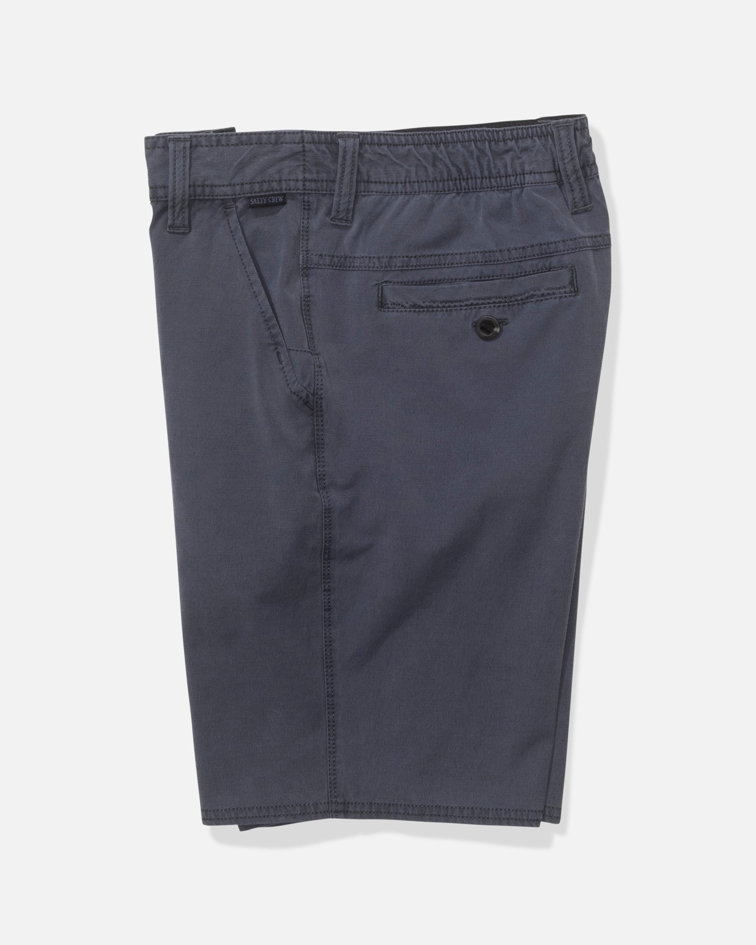 The Salty Crew Transom 17" Boys Overdye Short in Magnet is a pair of dark blue straight leg shorts with an elastic waistband, side and buttoned back pockets, plus comfy 4-way stretch fabric, shown folded on a white background.