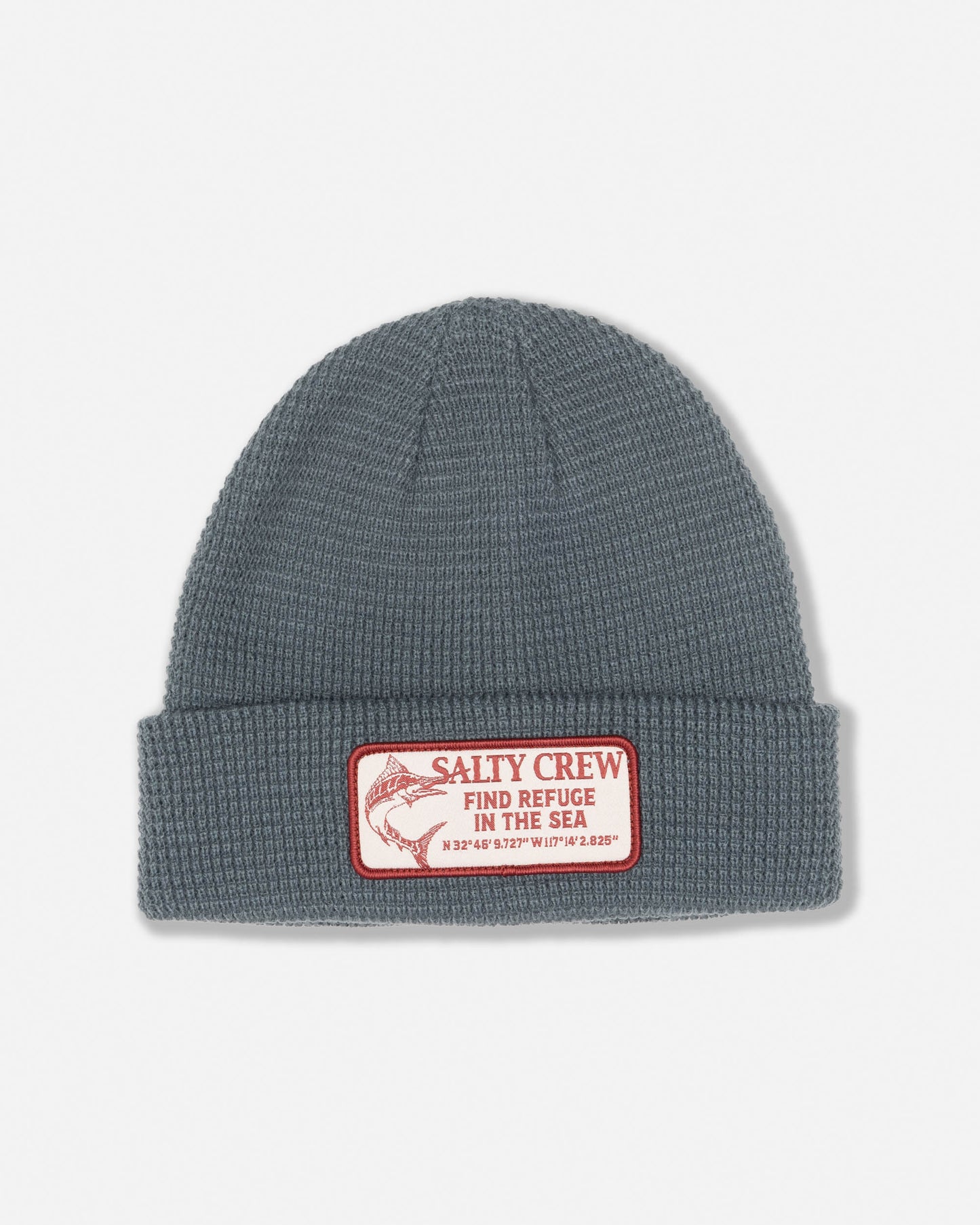 Introducing the Coastal Beanie - Mid Ocean by Salty Crew: a gray acrylic waffle knit beanie with a folded brim, featuring a rectangular woven patch displaying “SALTY CREW FIND REFUGE IN THE SEA,” geographic coordinates, and a fish illustration. Designed with six dart construction for a comfortable fit.