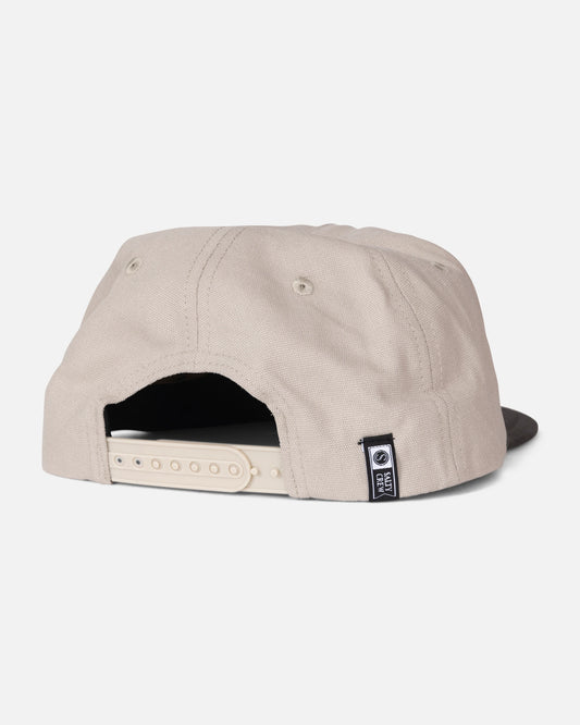 The Salty Crew Coastal Snapback - Grey/Tan is a mid crown, five-panel cotton hat in beige, shown from the back. It features an adjustable white strap, a small black and white Salty Crew fabric tag on the side, and two metal eyelets for ventilation.