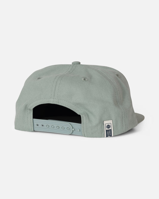 The Salty Crew Coastal Snapback - Iceberg is displayed from the back in a light green shade, highlighting its adjustable snapback strap and a small rectangular tag with a circular logo along the lower edge. Made from durable cotton canvas, this 5 panel hat is set against a plain white background.