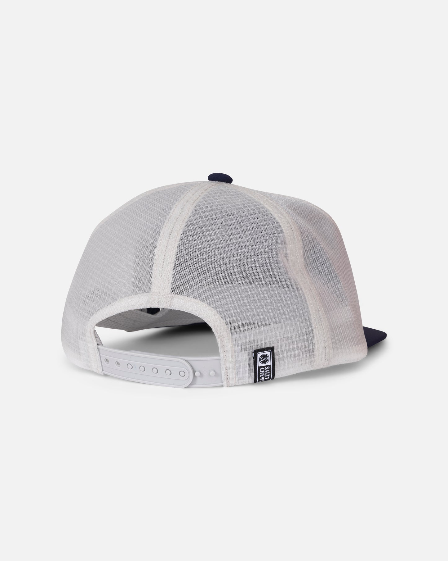 Back view of the Salty Crew Flagship Tech Trucker - Navy/Grey, an unstructured 5-panel trucker hat featuring white mesh, a navy blue brim, an adjustable snapback strap, and a small rectangular black and white patch near the closure, set against a plain light background.