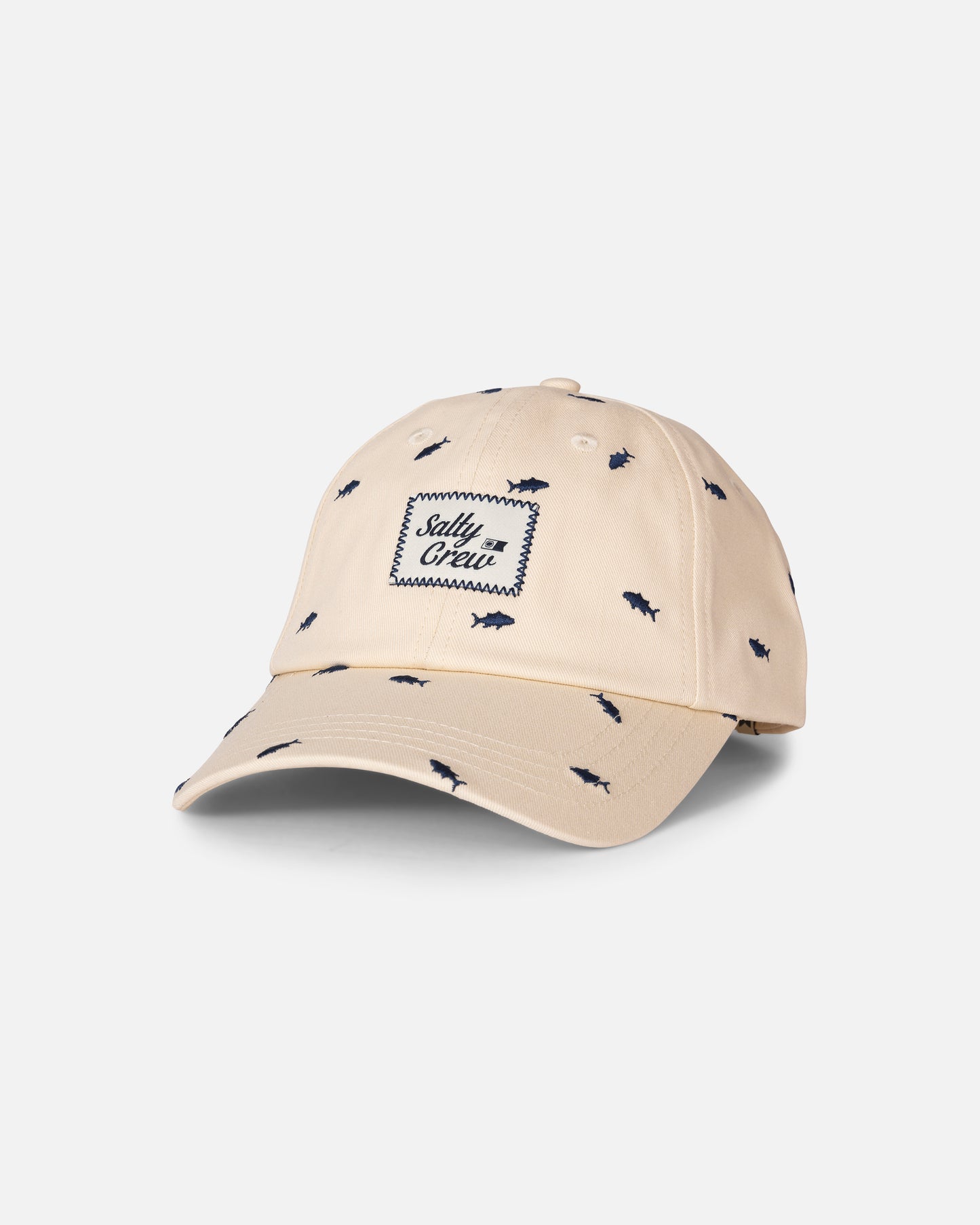 The Nice Catch Hat - Off White by Salty Crew is a cotton unstructured baseball cap featuring small blue shark patterns and a front patch with “Salty Crew” in blue script. This adjustable hat offers comfortable everyday wear and is pictured against a plain, light gray background.