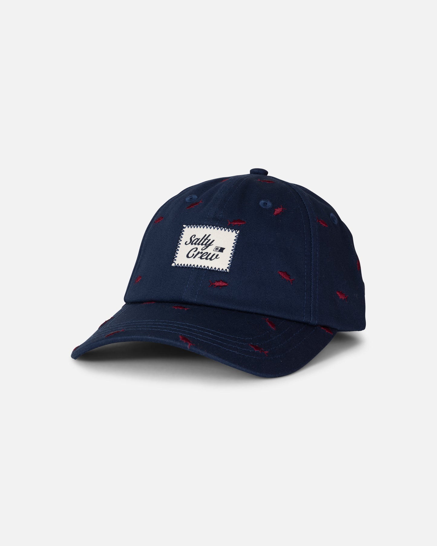 The Salty Crew Nice Catch Hat in True Navy is an unstructured cotton hat featuring small red fish patterns and a white embroidered patch on the front that reads “Salty Crew.” Designed for comfort, it includes a curved brim and stitched eyelets for breathability.