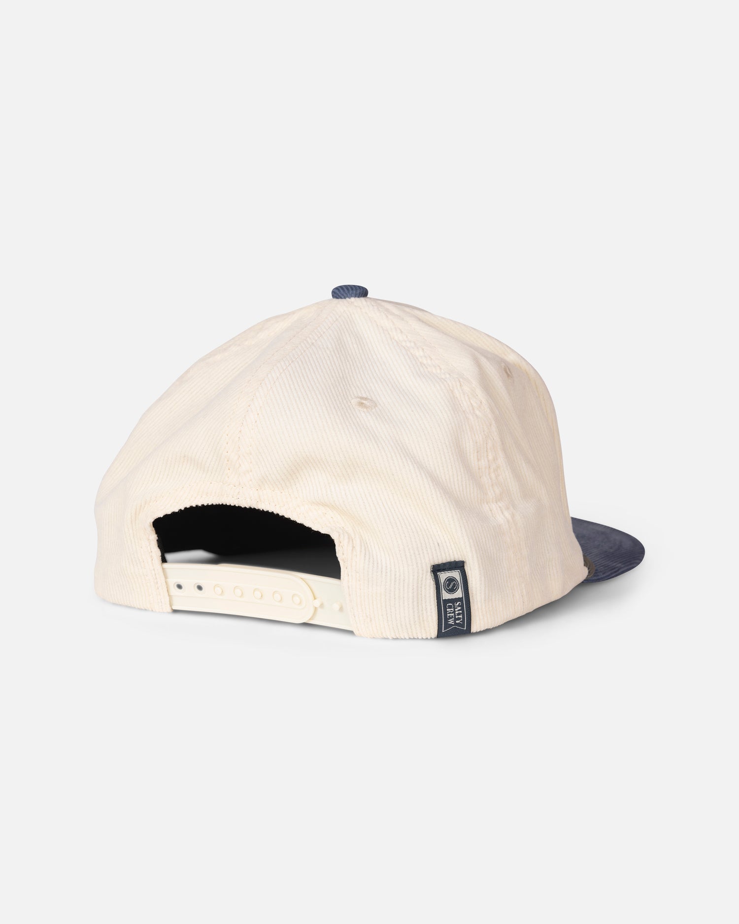 The Salty Crew Tarpon Snapback - Off White Blue features a classic baseball cap style in cream-colored cotton corduroy, paired with a navy blue brim. Viewed from the back, it showcases an adjustable snapback strap and a small stitched label on the side.