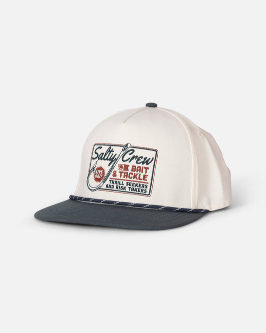 The Salty Crew Hooked Up Snapback in Off White/Navy is a cream-colored 5 panel cotton hat featuring a dark navy flat brim and a braided cord detail. The front panel displays a rectangular patch that reads “Salty Crew Bait & Tackle, Thrill Seekers and Risk Takers,” accompanied by a fish hook graphic.