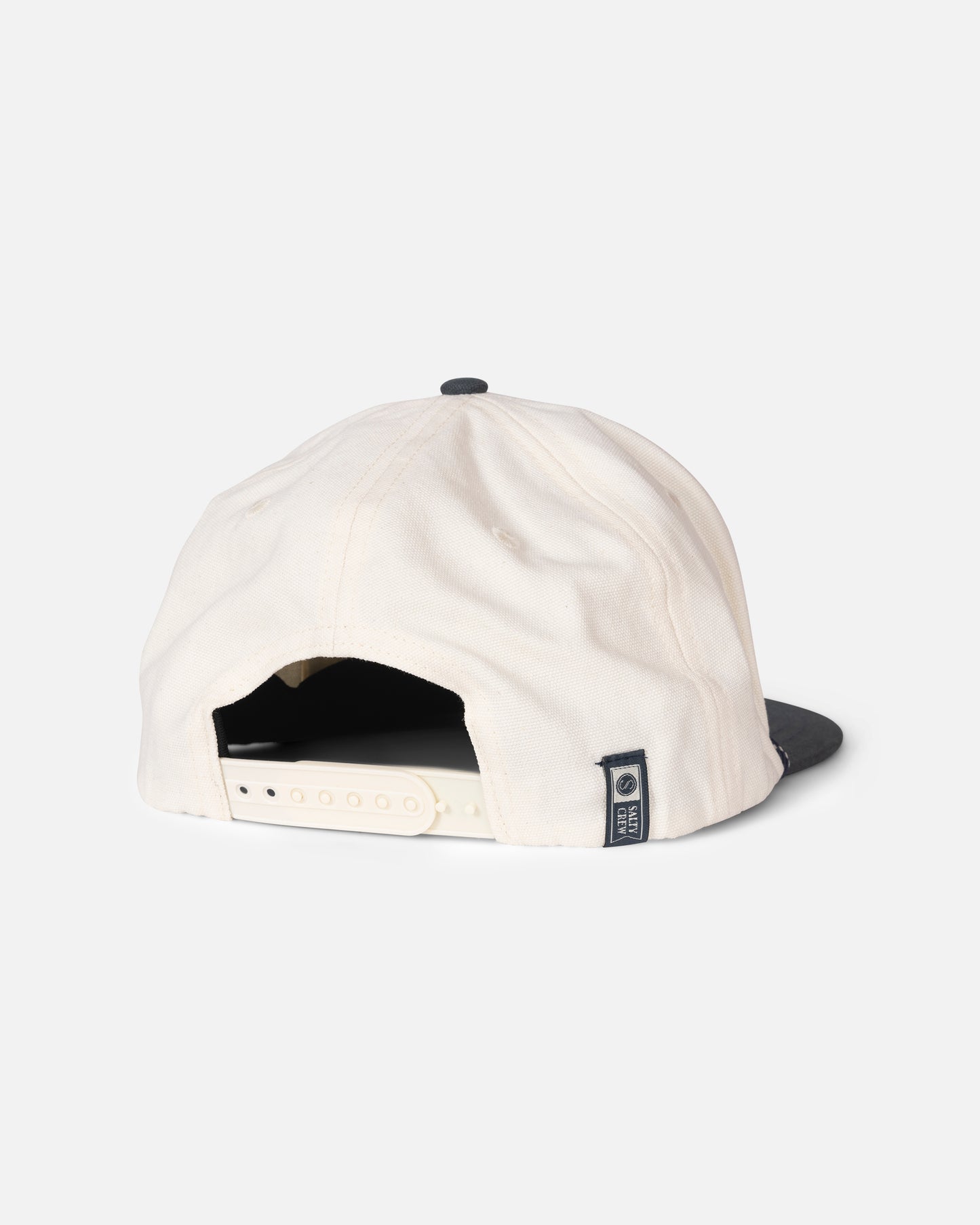 The Salty Crew Hooked Up Snapback - Off White/Navy is a white 5-panel cotton cap with a contrasting navy brim, shown from the back. It features an adjustable snap closure and a small fabric tag on the left side. The background is plain white.