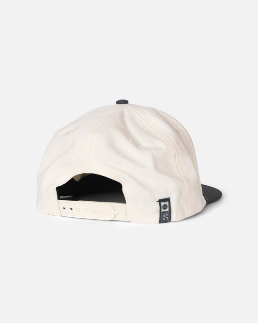 The Salty Crew Hooked Up Snapback - Off White/Navy is a white 5-panel cotton cap with a contrasting navy brim, shown from the back. It features an adjustable snap closure and a small fabric tag on the left side. The background is plain white.