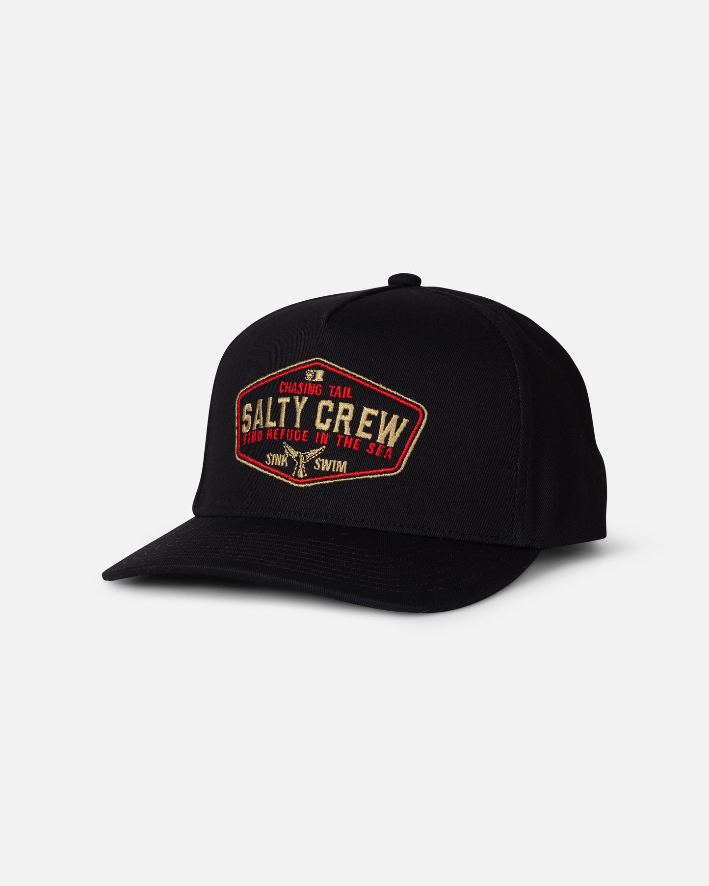 The Salty Crew Tailfin Snapback – Black is a black cotton snapback baseball cap with a curved brim and a high crown, featuring a striking red and gold embroidered artwork patch on the front that displays the Salty Crew name along with smaller text. The hat is showcased against a light gray background.