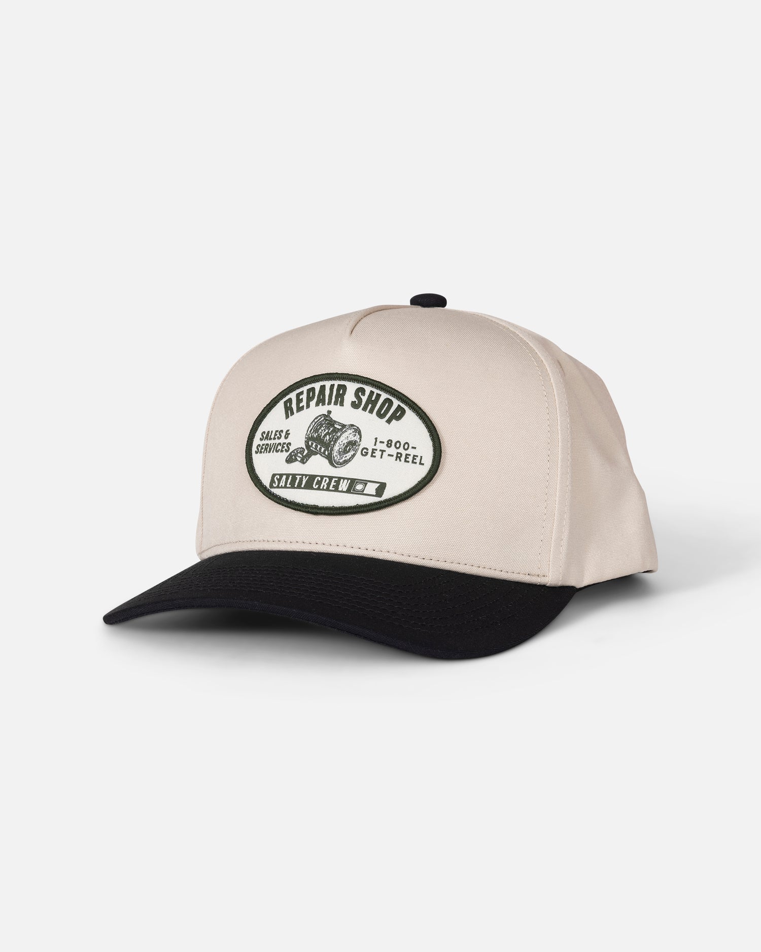 The Salty Crew Reel Repair Snapback in Off White/Black is a structured 5-panel baseball cap made from durable cotton canvas, featuring a snapback closure. The front patch displays “Repair Shop,” “Salty Crew,” “1-800-GET-REEL,” and “Reel & Engine Services” along with a reel graphic.