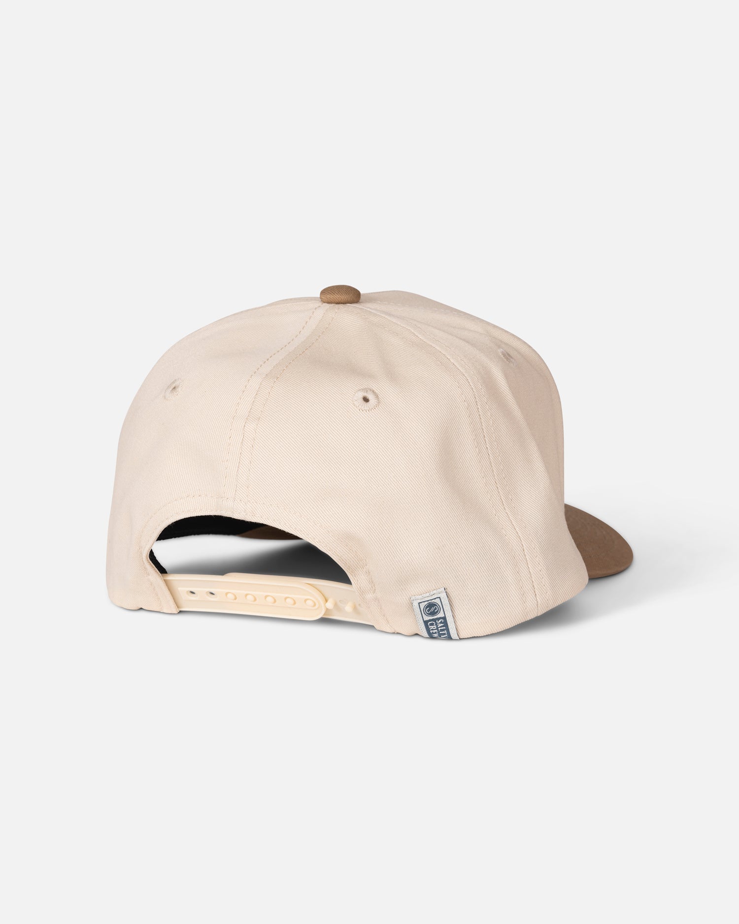 The Salty Crew Coordinates Snapback - Off White/Tan is a beige cotton baseball cap with a brown brim, viewed from the back to showcase its adjustable snapback closure and small sewn label near the opening. This high crown hat delivers classic style and comfort, making it perfect for any casual outing.