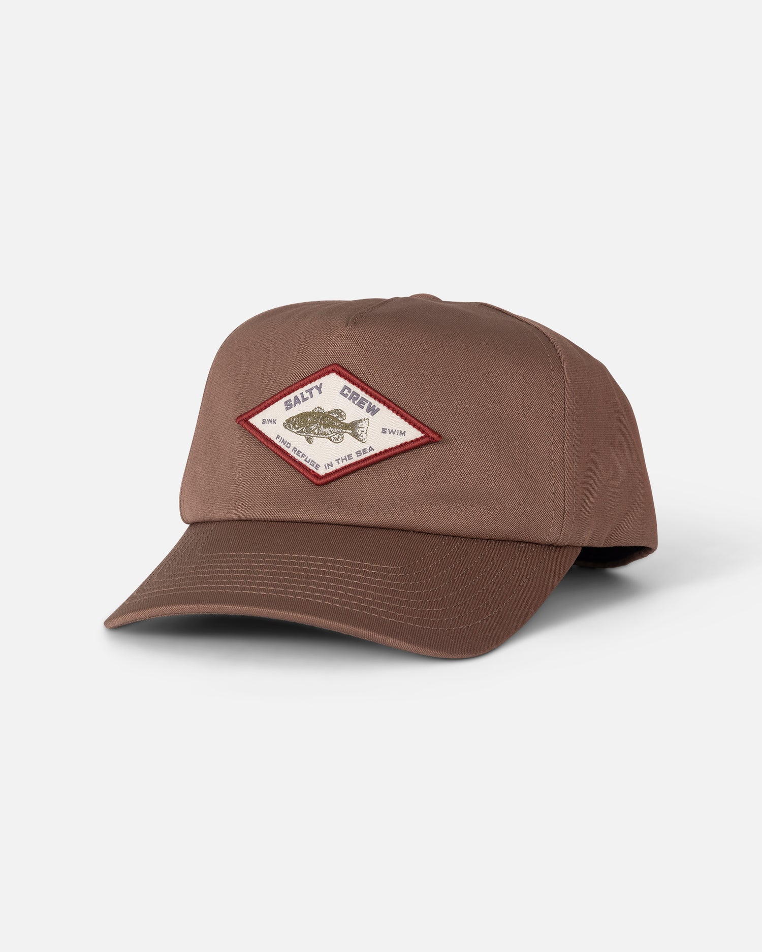 The Badge Snapback - Washed Brown by Salty Crew is a brown 5-panel hat made from durable cotton canvas, featuring a snapback closure and a diamond-shaped patch on the front with text and an outlined fish design in red, shown against a plain white background.