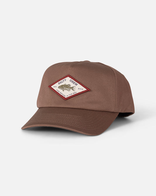 The Badge Snapback - Washed Brown by Salty Crew is a brown 5-panel hat made from durable cotton canvas, featuring a snapback closure and a diamond-shaped patch on the front with text and an outlined fish design in red, shown against a plain white background.