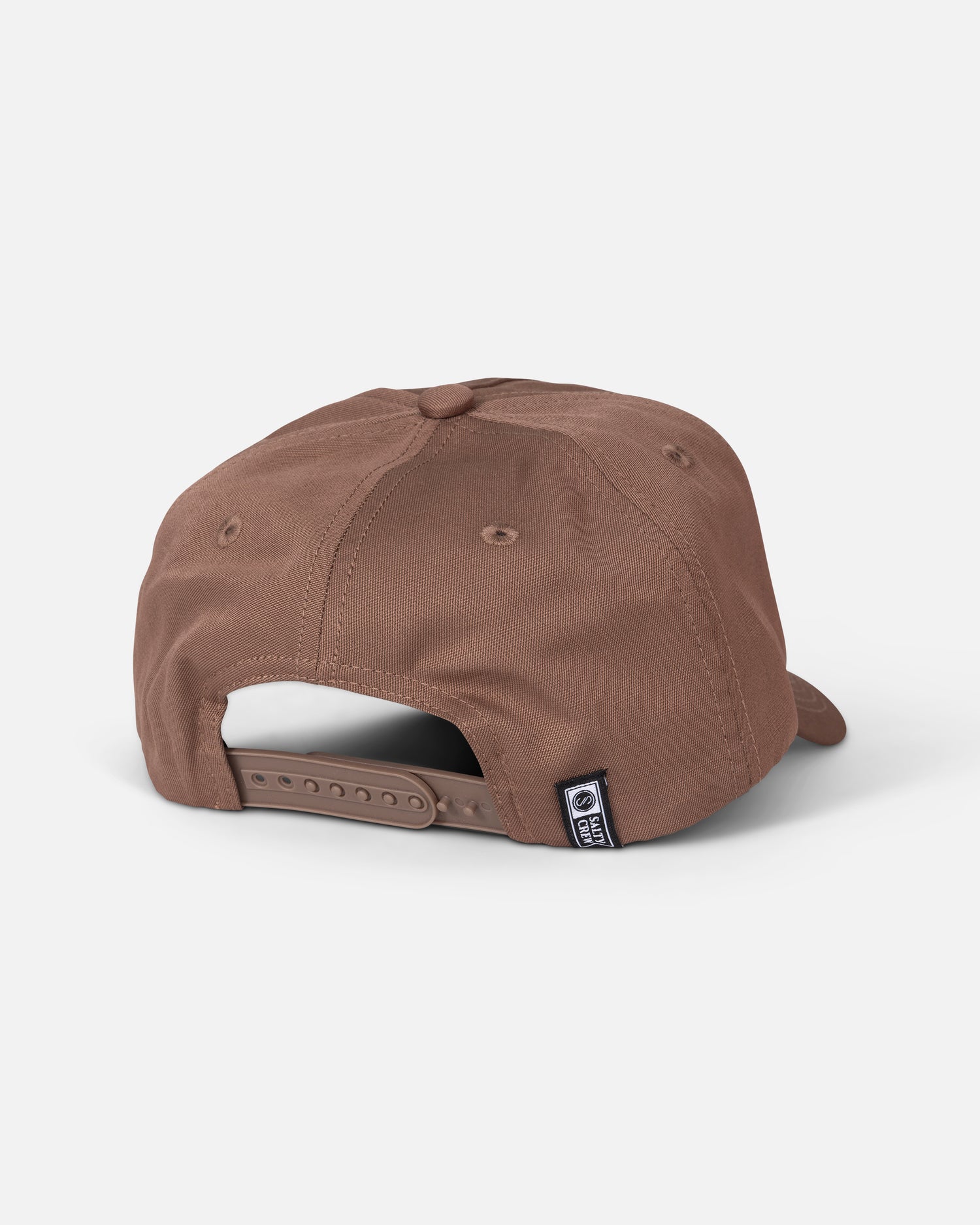 The Salty Crew Badge Snapback in Washed Brown is shown from the back, featuring an adjustable snapback closure and a small black label with a white logo on the left side near the opening. Made from durable cotton canvas, this 5 panel hat is displayed against a plain white background.
