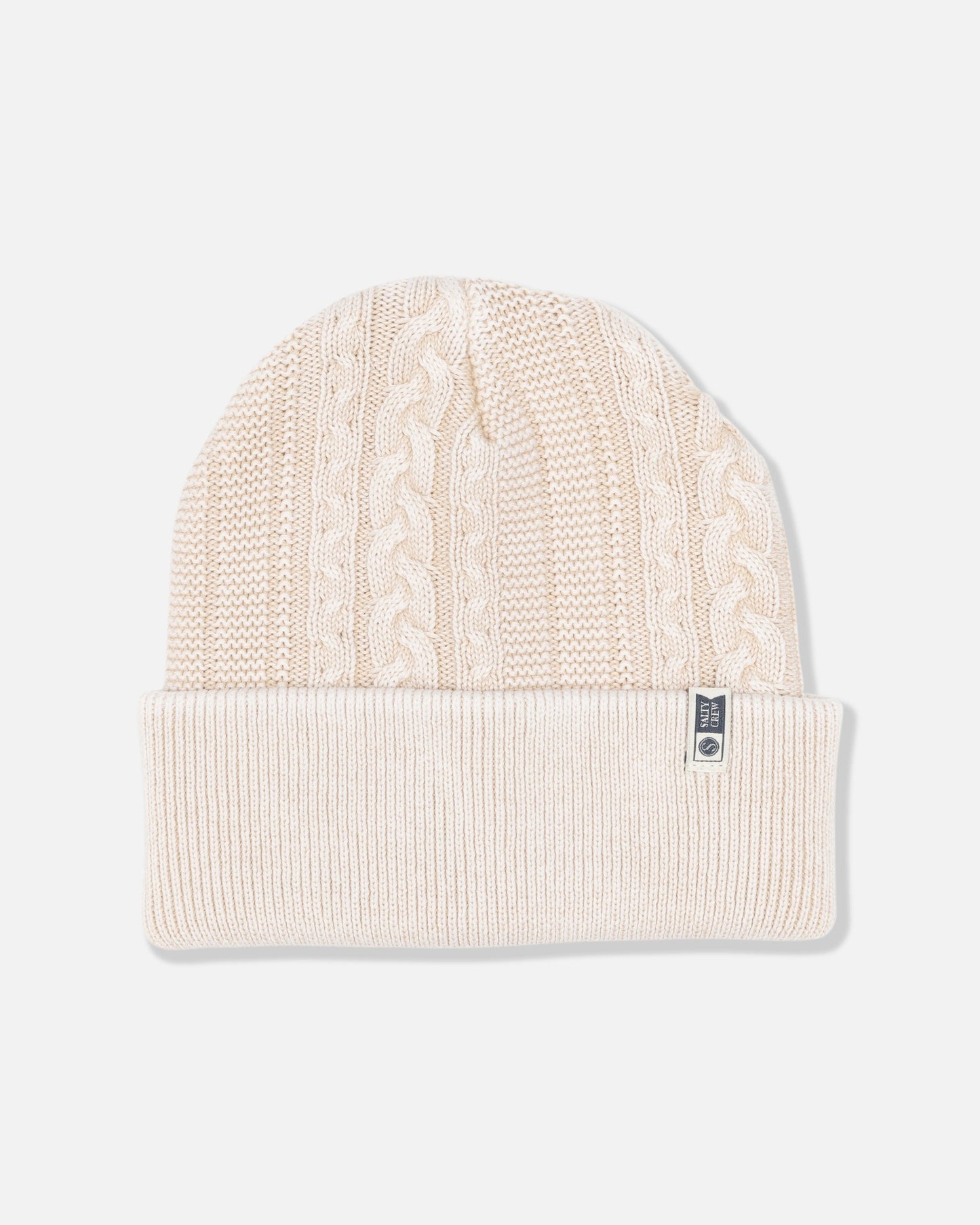The Salty Crew Fisherman Beanie - Stone is a cream-colored, cable knit style with a folded brim, featuring a vintage wash finish and a small fabric tag on the cuff.
