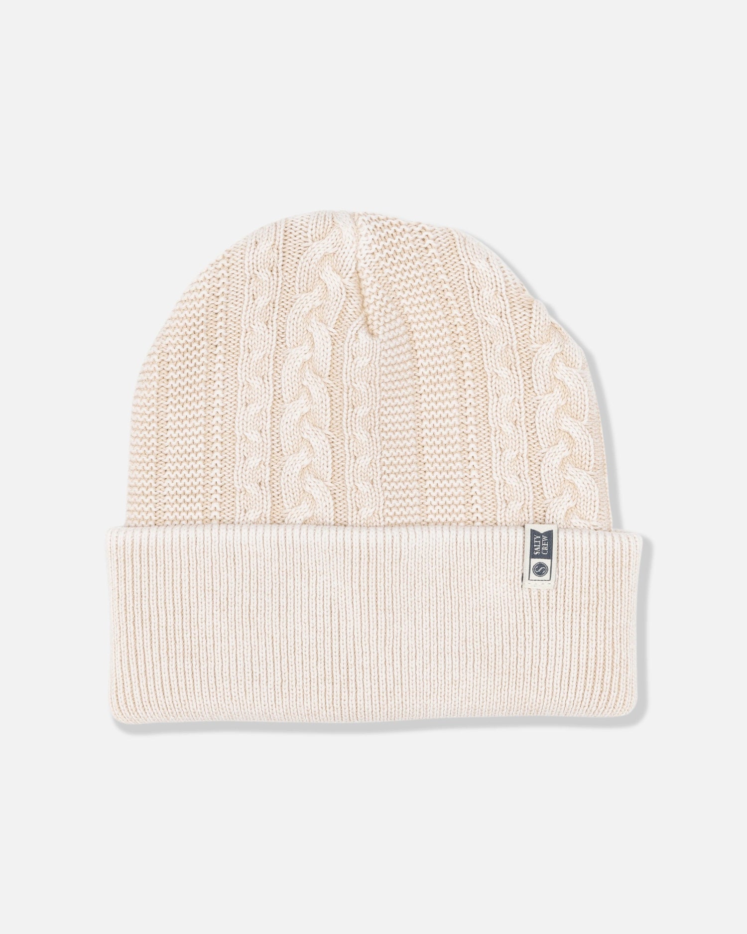 The Salty Crew Fisherman Beanie - Stone is a cream-colored, cable knit style with a folded brim, featuring a vintage wash finish and a small fabric tag on the cuff.