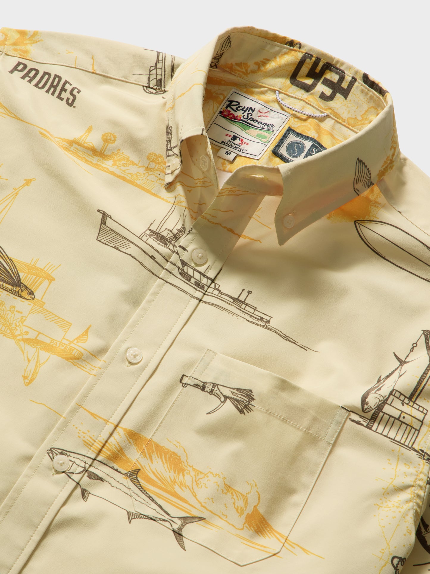 The Padres x Reyn Spooner UV Button Up - Bone by Salty Crew is a cream short-sleeve shirt featuring yellow and black illustrations of ships, planes, a fish, and “PADRES” text. Designed in collaboration with Reyn Spooner for the San Diego Padres, this button-up includes a front pocket and an embroidered label at the collar.