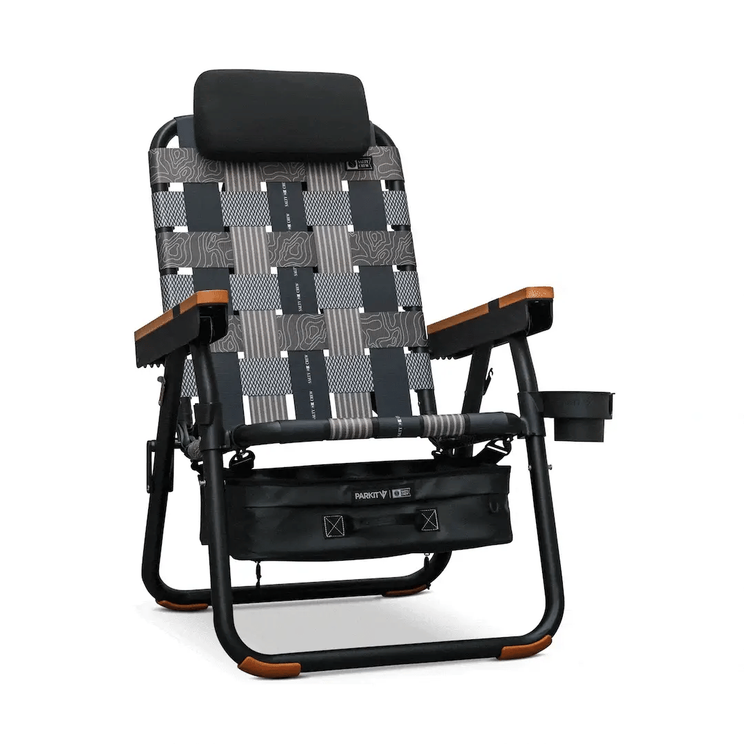 Parkit x Salty Crew Eclipse Recliner featuring woven straps, wooden armrests, a black headrest, a cup holder, and a detachable storage bag underneath the reclining camp chair.