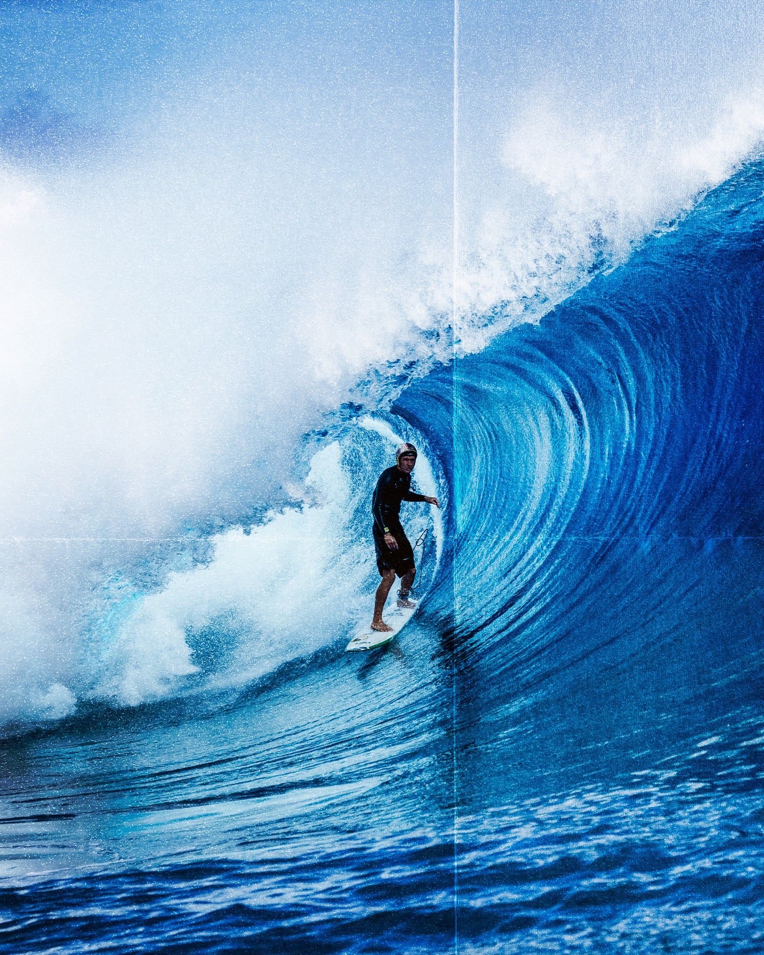 A surfer in Salty Crew's Portal 21" Boardshort - Black rides inside the barrel of a large blue ocean wave, surrounded by water spray and white foam under a clear sky.