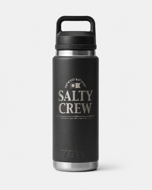 The Salty Crew Yeti x Salty Crew Rambler 26 Oz Black Water Bottle features a handle, silver base, and white SALTY CREW text with coordinates on the front. Made of durable stainless steel with vacuum insulation for lasting performance.