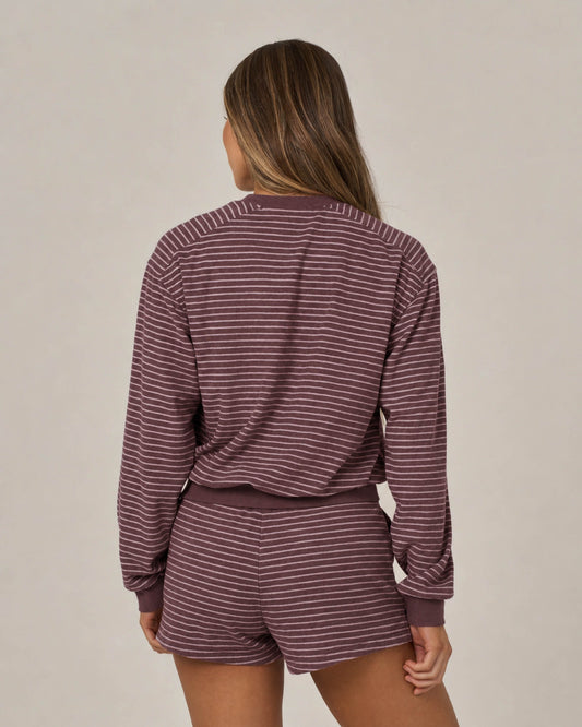 A person with long hair is standing with their back to the camera, wearing the Salty Crew Leeward Crew in maroon—a matching maroon and white stripe crew neck long-sleeve top and shorts set featuring a branded patch—against a plain background.