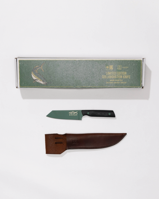 A Salty Crew Leucadia x Salty Crew 5” Snapper Utility Knife with a black handle rests above a handmade leather sheath. Above them is a green rectangular box labeled "Limited Edition Utility Knife" with a fish illustration.