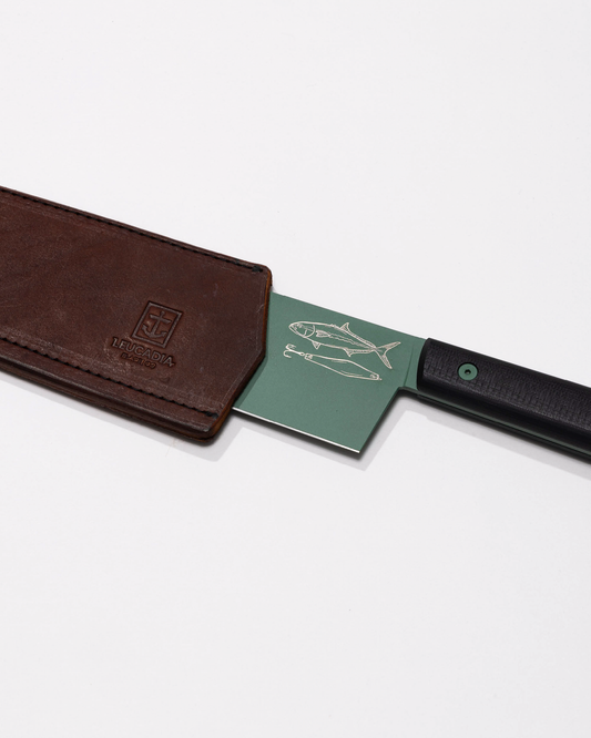 The Leucadia x Salty Crew 7” Bunka Knife by Salty Crew features a limited edition green AEB-L Swedish stainless steel blade with engraved fish, partly sheathed in brown leather with an embossed logo, shown on a white background.