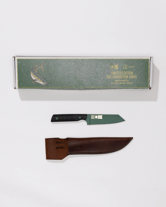 The Leucadia x Salty Crew 5” Snapper Utility Knife by Salty Crew features a Detroit Diesel Green blade, black handle, handmade leather sheath, and comes in a green box with gold fish illustration, displayed on a white surface.
