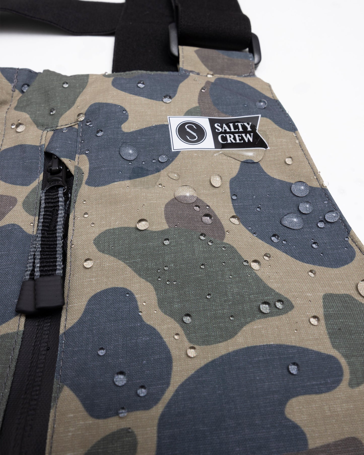Close-up of Salty Crew’s Long Range Tech Bib in Sand Camo: ultra-waterproof, durable camo fabric with water droplets, Salty Crew logo patch, and black zipper.