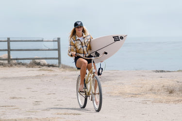 Shot of model riding a bike with their surfboard 